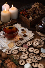 Wooden runes are lying on the table among the papers with notes. There is a mug of tea next to it. Astrology and esotericism.