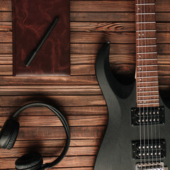 Headphones, notebook and guitar on a wooden table. Musical theme.