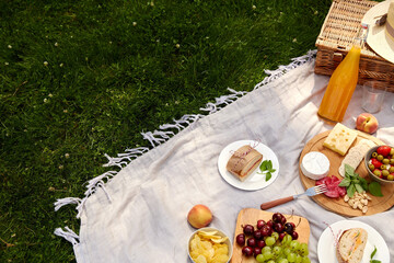 leisure, food and drinks concept - close up of snacks and picnic basket on blanket on grass at summer park