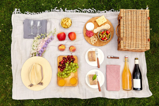 leisure, food and drinks concept - close up of snacks and picnic basket on blanket on grass at summer park