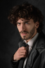 Young man with beard in white shirt and black leather coat against black background. High quality photo