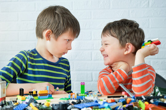 two brothers sit at the table and assemble the designer, build from toy cubes. One child laughs, the other looks serious. Fun collaborative activity. The boys are friends, busy with a common cause
