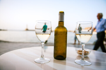 A bottle of white wine with two glasses in a harbour cafe in a summer night in Crete.