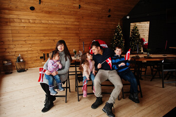 Obraz na płótnie Canvas Family with Denmark flags inside wooden house sitting by table. Travel to Scandinavian countries. Happiest danish people's .