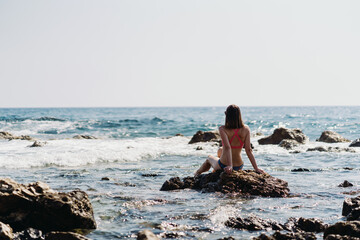 Happy young woman enjoying freedom on vacation while sitting on the coast rocks enjoying sea and blue sky view