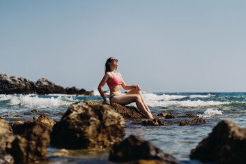 Fototapeta na wymiar Happy young woman enjoying freedom on vacation while sitting on the coast rocks enjoying sea and blue sky view