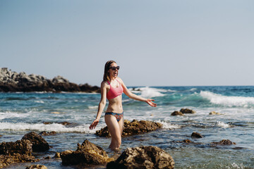 Happy young woman enjoying freedom with open hands on vacation while standing on the coast rocks enjoying sea and blue sky view