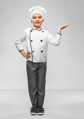 cooking, culinary and profession concept - happy smiling little boy in chef's toque and jacket holding something imaginary on hand over grey background