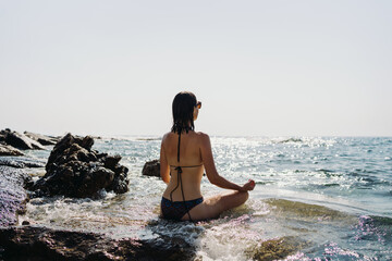 Happy young woman enjoying freedom on vacation while sitting on the coast rocks enjoying sea and blue sky view