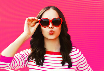 Portrait of beautiful young brunette woman blowing her lips wearing red heart shaped sunglasses on...