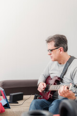 50-year-old concentrated man follows teacher's instructions via tablet to learn to play electric guitar at home
