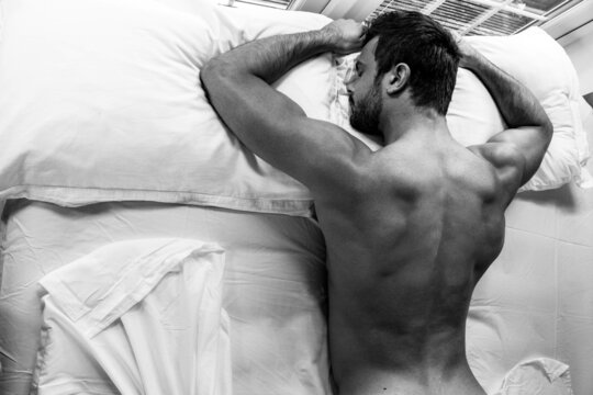 Handsome naked muscular man with sleeping face down on bed with partial backside and room for copy