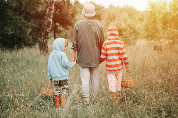 little kids mushroom pickers go to the forest by the hand with their grandmother. family of...