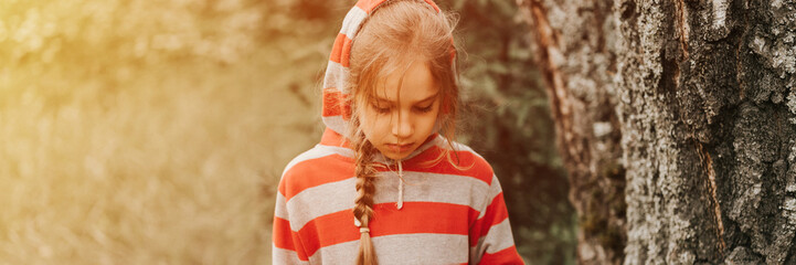 portrait face of upset or focused thoughtful scowl eight year old kid girl in hood of striped...