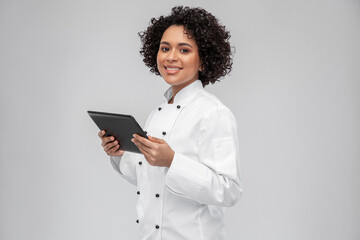 cooking, culinary and people concept - happy smiling female chef in white jacket with tablet pc computer over grey background
