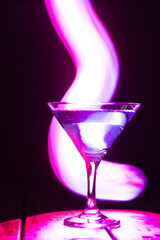 triangular glass with a blue cocktail on a dark background and neon lighting.