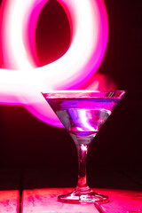 triangular glass with a blue cocktail on a dark background and neon lighting.