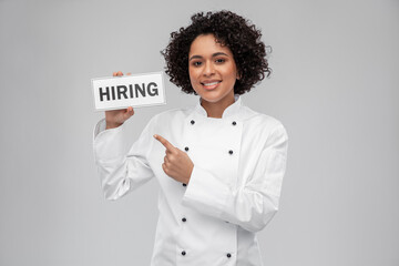 job, work and employment concept - happy smiling female chef in white jacket holding hiring sign over grey background