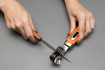 female hand sharpens a kitchen knife with a sharpener