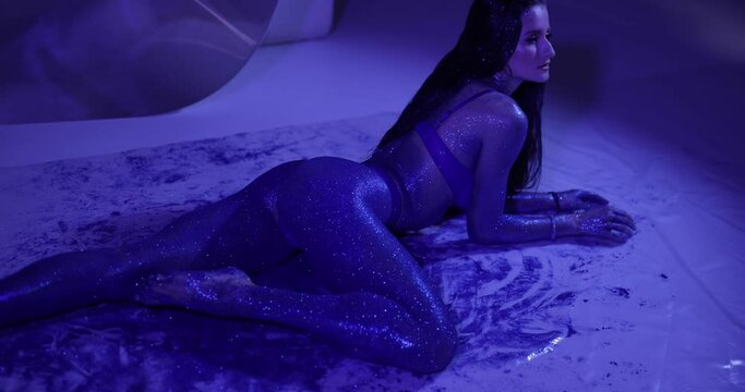 Attractive woman with blue glitter on the body posing lying in a studio