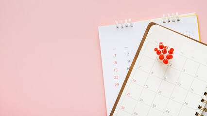 many red thumbtacks pin on 1st date of month on opened planner with monthly calendar and sweet pink...