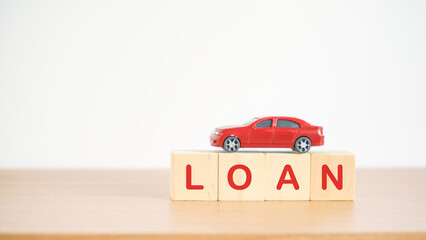 red miniature car on wooden block with LOAN word, on wood desk including copy space, vehicle loan, saving money for car, trade automobile for cash, finance concept