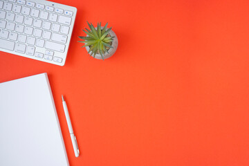 Workspace with office supplies, red background. On the desktop keyboard, flower, notepad, pen. Flat lay, Top view