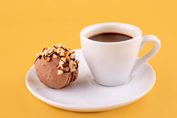 cup of coffee and chocolate macaroon on saucer on yellow background