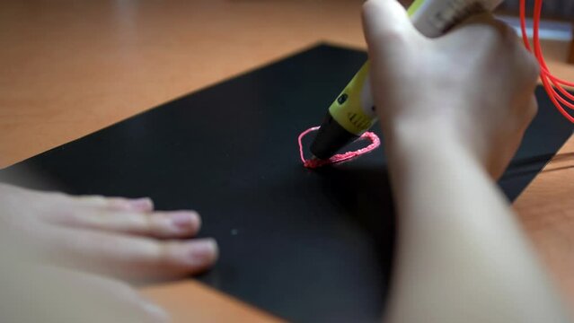 A girl draws a heart with a 3D pen. The daughter creates a beautiful pink keychain as a gift for mom on mother's day or for dad on father's day. close-up work 3d pens.
