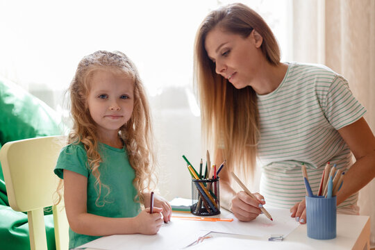 Portrait of daughter and mother drawing together Spend Leisure time play fun at home. Caucasian blonde pregnant mother helps kid child preschool girl daughter doing homework.