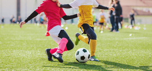 School girl and boy playing soccer game. Kids having fun and playing football match. Girl in pink soccer uniform kicking ball