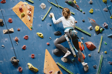 Teenage girl at indoor climbing wall. Kid having fun at bouldering wall. Child learning at climbing...