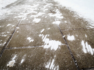 Wind made snow stains on tiled dark pavement surface