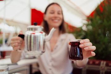 Smiling woman pouring tea from a silver pot at a Turkish breakfast on a terrace