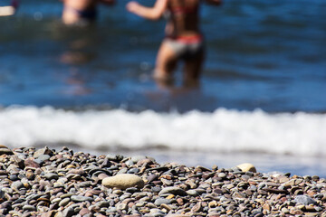 Texture of coastal gravel with unrecognizable people having fun in the sea in the background, concept of lifestyle and fun.