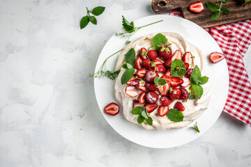 delicious homemade Pavlova cake with fresh strawberries and whipped cream. Female baker decorating delicious meringue cake, top view. place for text