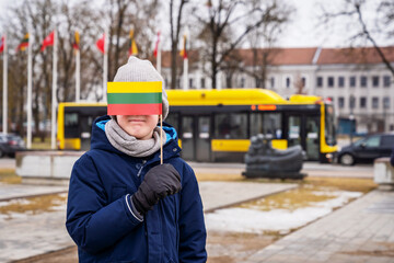 Boy proudly holds tricolour Lithuania flag in town square. Family celebrating public holiday -...