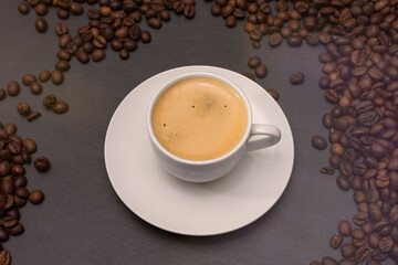 Obraz premium white cup with espresso coffee on a saucer with coffee beans on a dark background