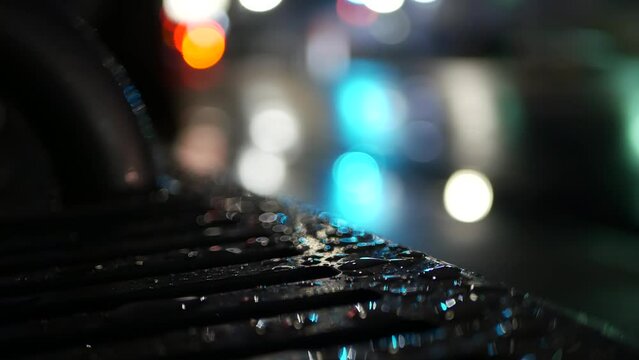 Car traffic lights bokeh, reflection on bus stop bench in rainy weather. Water rain drops on wet metal, city street in Clifornia, USA. Rainfall at night. Defocused abstract Seamless looped cinemagraph