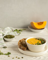 Pumpkin cream soup in a white bowl decorated with cesam seeds and cilantro nearby slice of bread
