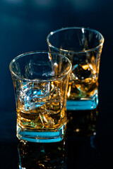 Glass of amber scotch whiskey and ice on a blue background
