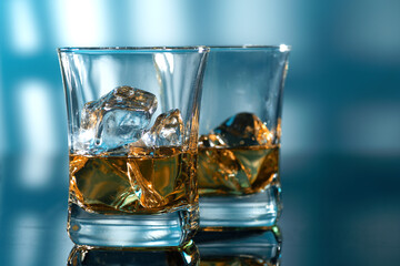 Glass of amber scotch whiskey and ice on a blue background