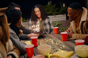 Birthday girl smiling as group of diverse young adults celebrate her birthday at rooftop party with cake