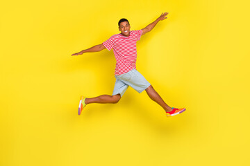 Fototapeta na wymiar Full length profile side photo of guy jump raise hands aside run wear red striped footwear isolated over yellow color background