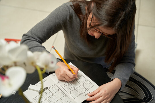 Woman playing sudoku game at home in a game book , alone