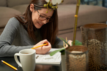 Woman playing sudoku game at home in a game book, alone