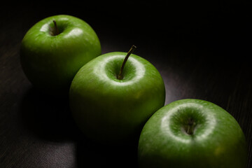 Three green fresh Granny Smith apples lie in a row on a dark background.