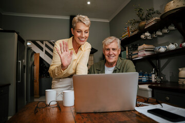 Caucasian senior couple waving on video call in kitchen