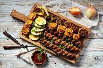 Assorted kebabs with grilled vegetables and herbs. Appetizing fried meat, corn, zucchini and mushrooms. Top view. Copy space