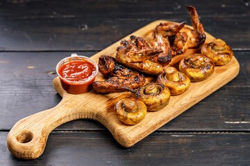 Grilled chicken wings and champignons on a wooden cutting board. Copy space